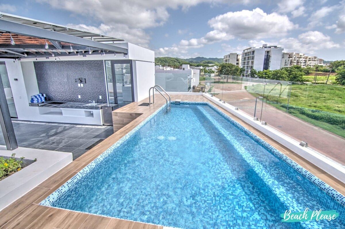 A rooftop swimming pool with a modern design, surrounded by a glass railing and a view of the cityscape.