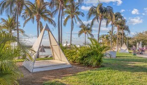 A grassy area with a white pyramid structure, palm trees, and a body of water in the background.