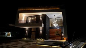 Een modern herenhuis met twee verdiepingen en een balkon, verlicht door buitenverlichting.