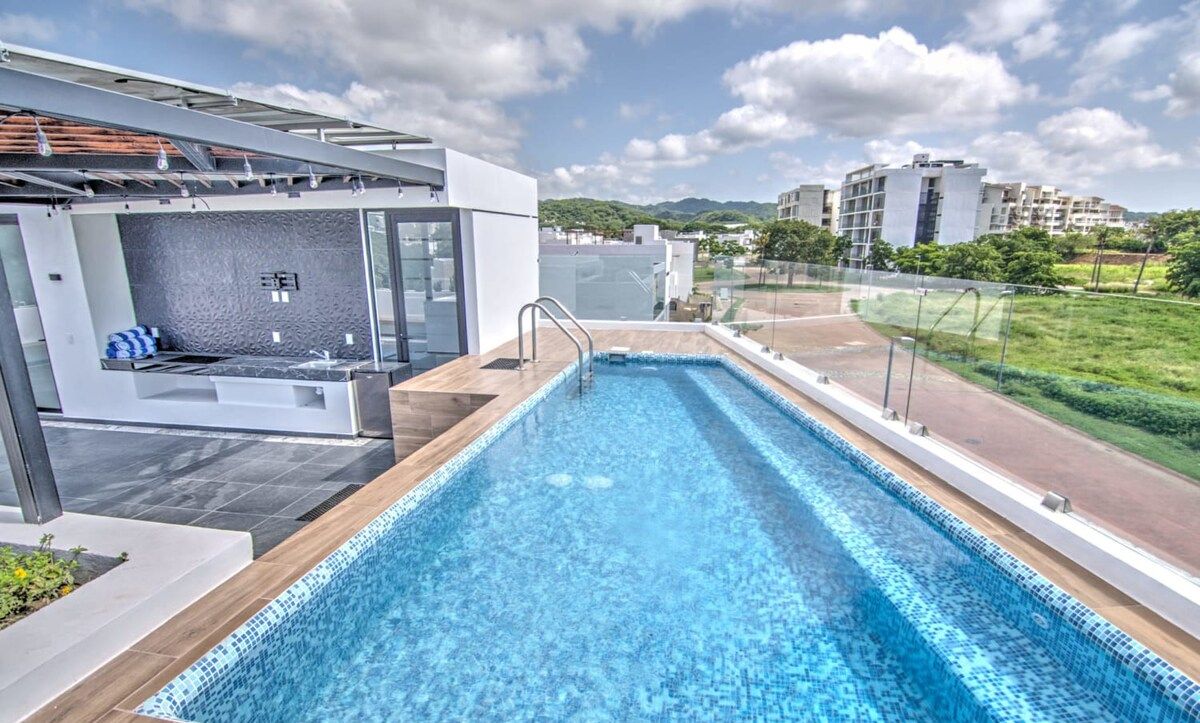 Une piscine sur le toit, dotée d’un design moderne, entourée d’une rambarde en verre et offrant une vue sur le paysage urbain.
