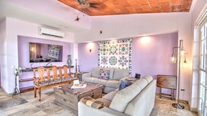 A living room with a sofa, a wooden bench, a coffee table, and a patterned tapestry on the wall.