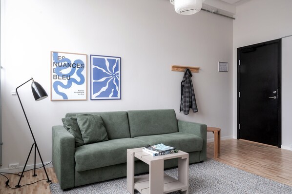 A modern living room with a green sofa, a small side table with books, a floor lamp, and two framed artworks on the wall. - South Studios by Daniel & Jacob's (København)