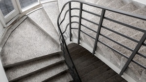 A spiral staircase with metal railings and a view of parked cars outside.