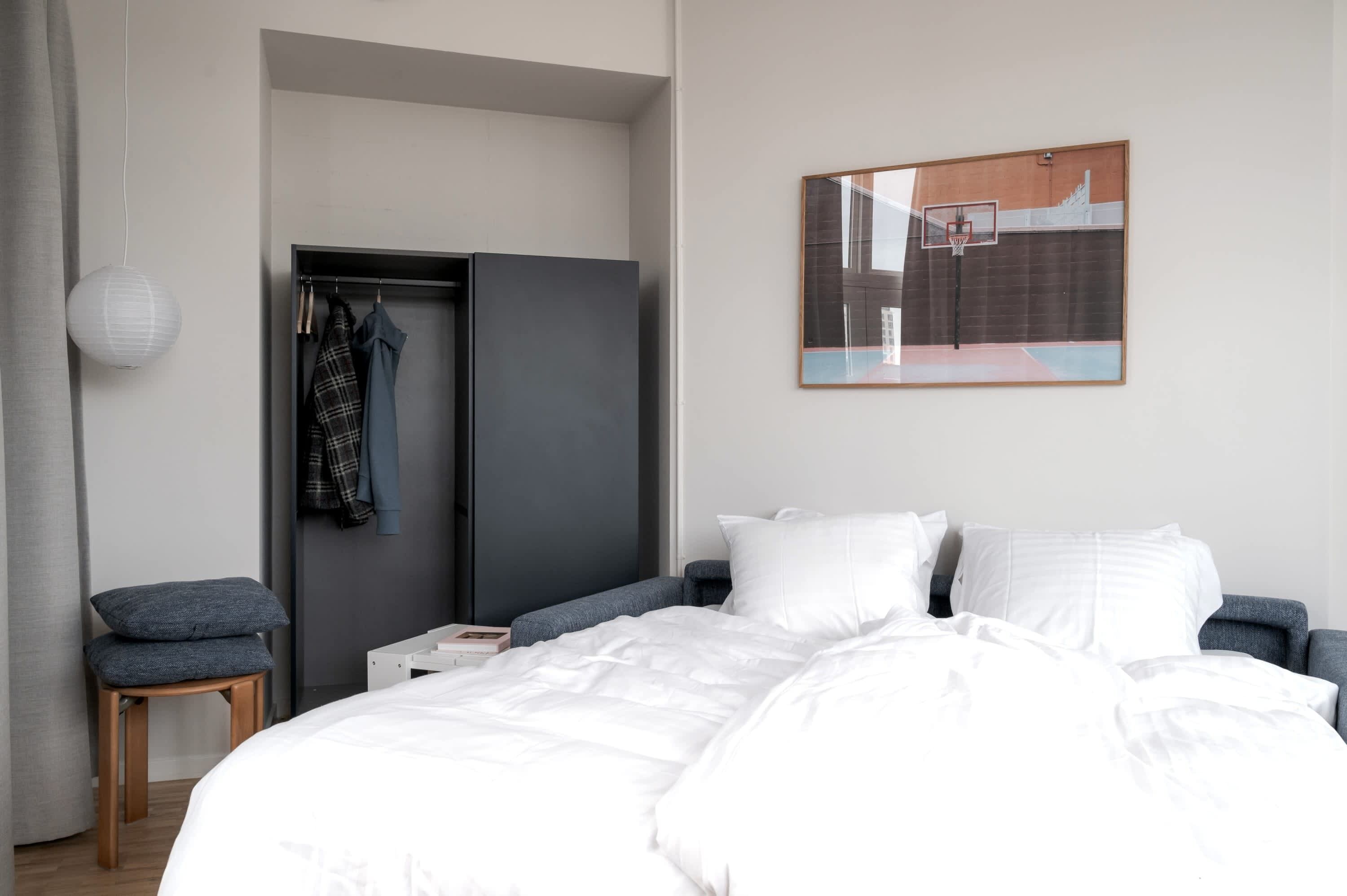 Een moderne slaapkamer met een bed, een kledingkast, een stoel en een kunstwerk aan de muur.