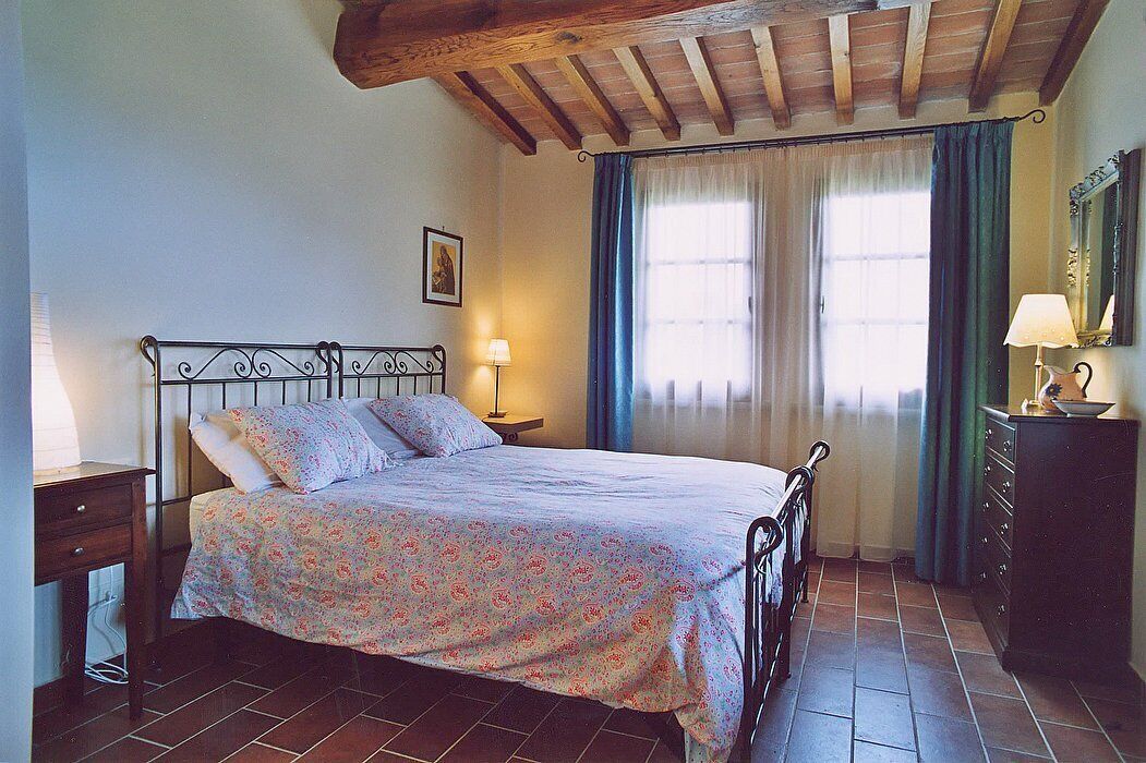 Un dormitorio con cama, mesita de noche, cómoda y ventana con cortinas.