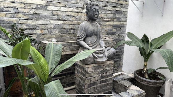 Seated Buddha statue surrounded by lush greenery in a serene, garden setting.