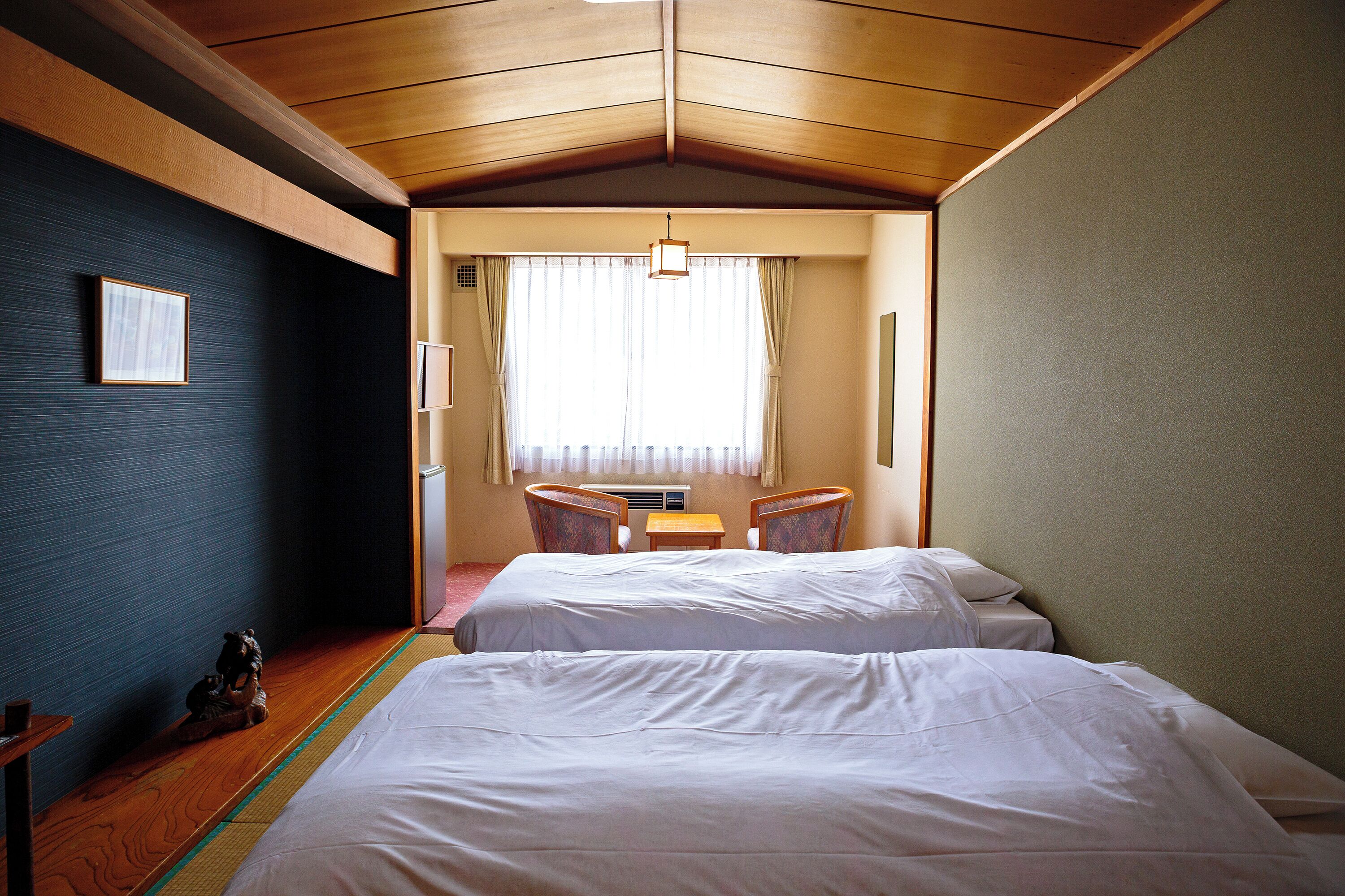 A hotel room with two beds, a small table, chairs, and a window with curtains.