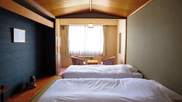Una habitación de hotel con dos camas, una mesita pequeña, sillas y una ventana con cortinas.