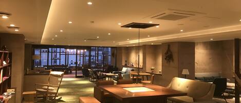 A spacious hotel lobby with a large seating area, a fireplace, and a view of the cityscape through large windows.
