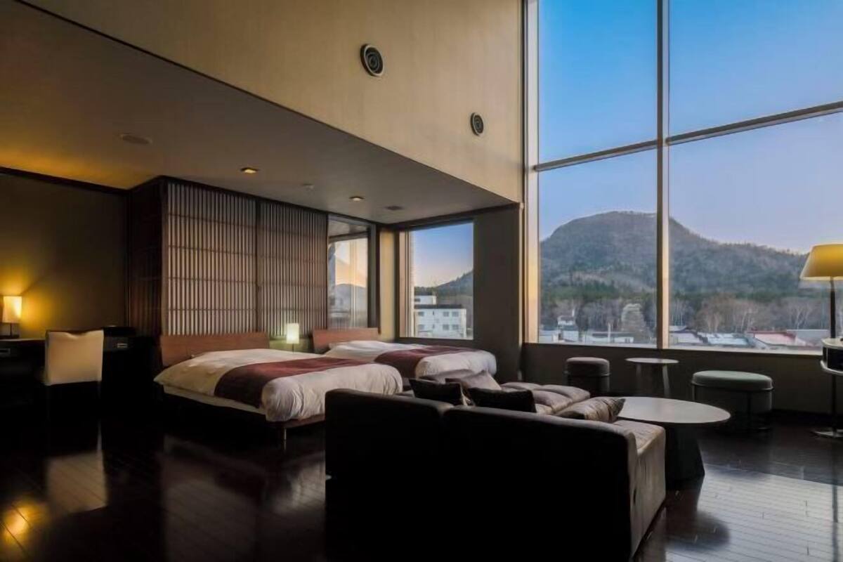 Une chambre d’hôtel moderne avec une grande fenêtre, un lit, un canapé et une petite table.