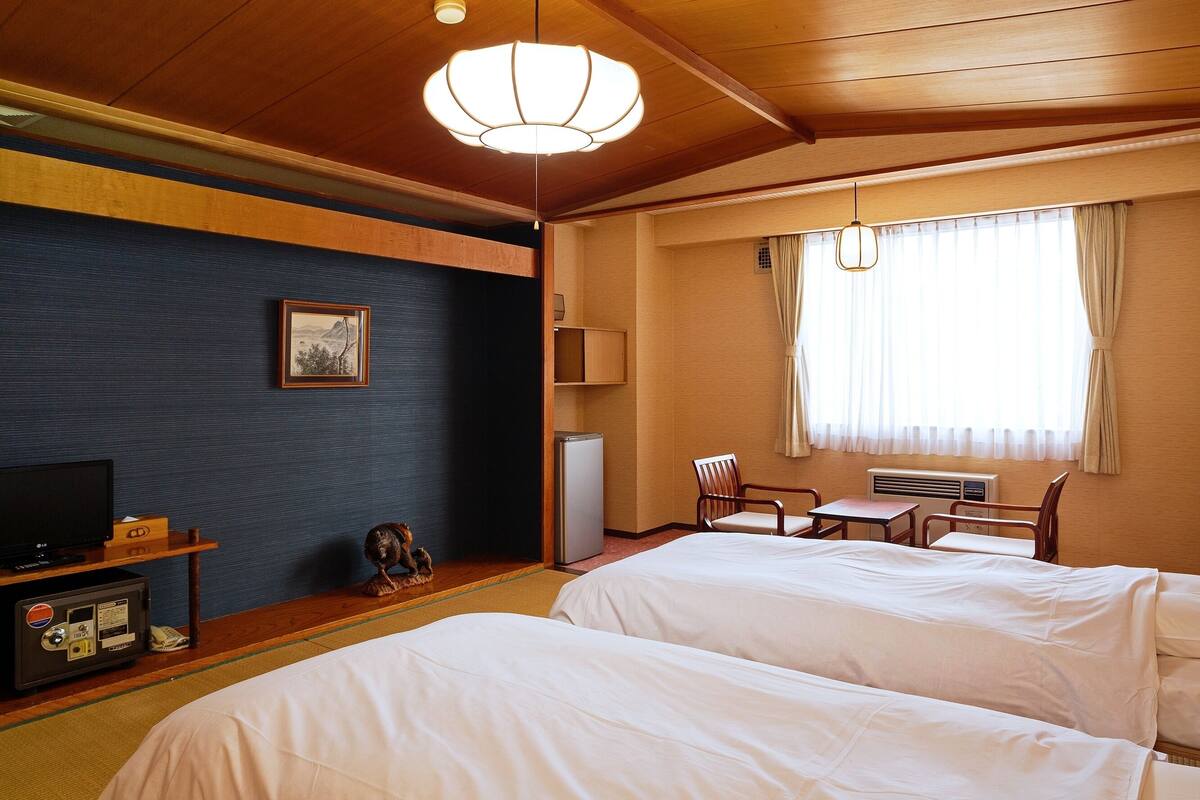 Une chambre d’hôtel avec deux lits, une télévision, une petite table, une chaise et une fenêtre avec des rideaux.