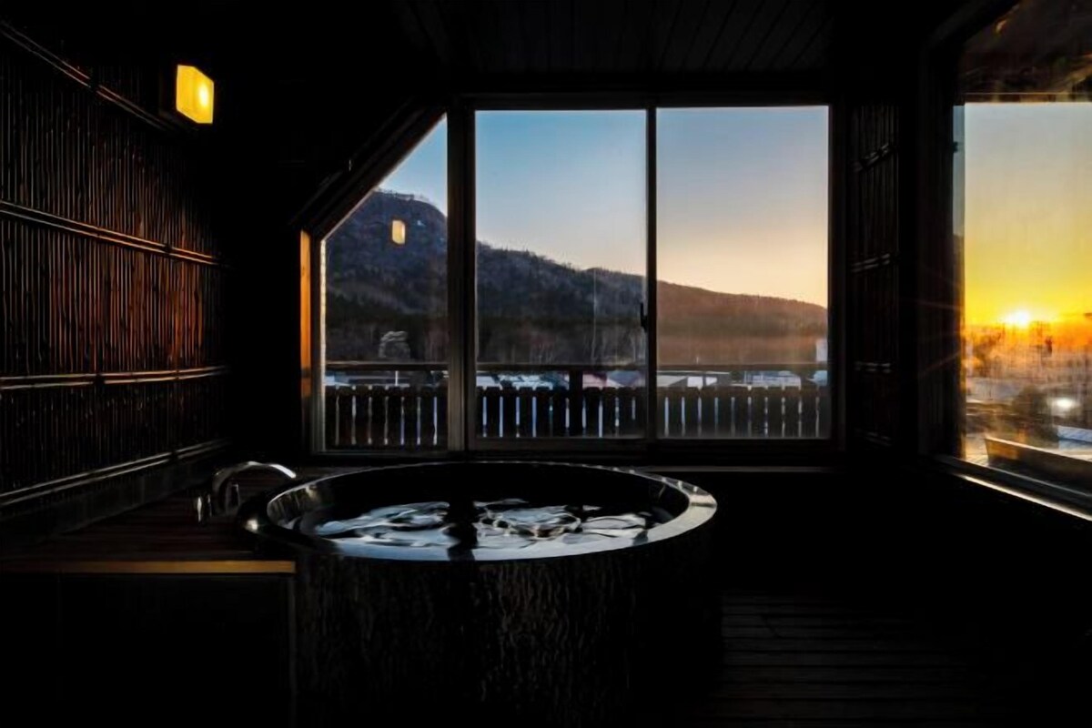 A room with a large window, a hot tub, and a view of a mountain.