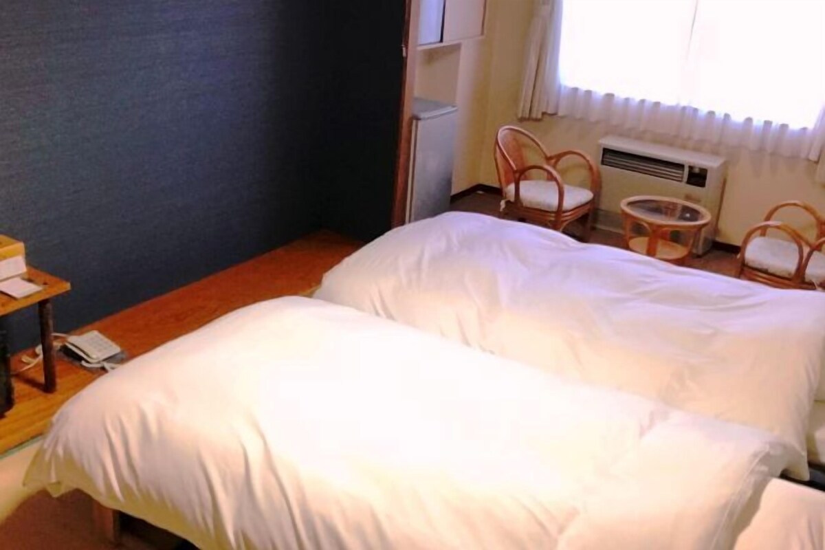A hotel room with two beds, a small table, and a chair.