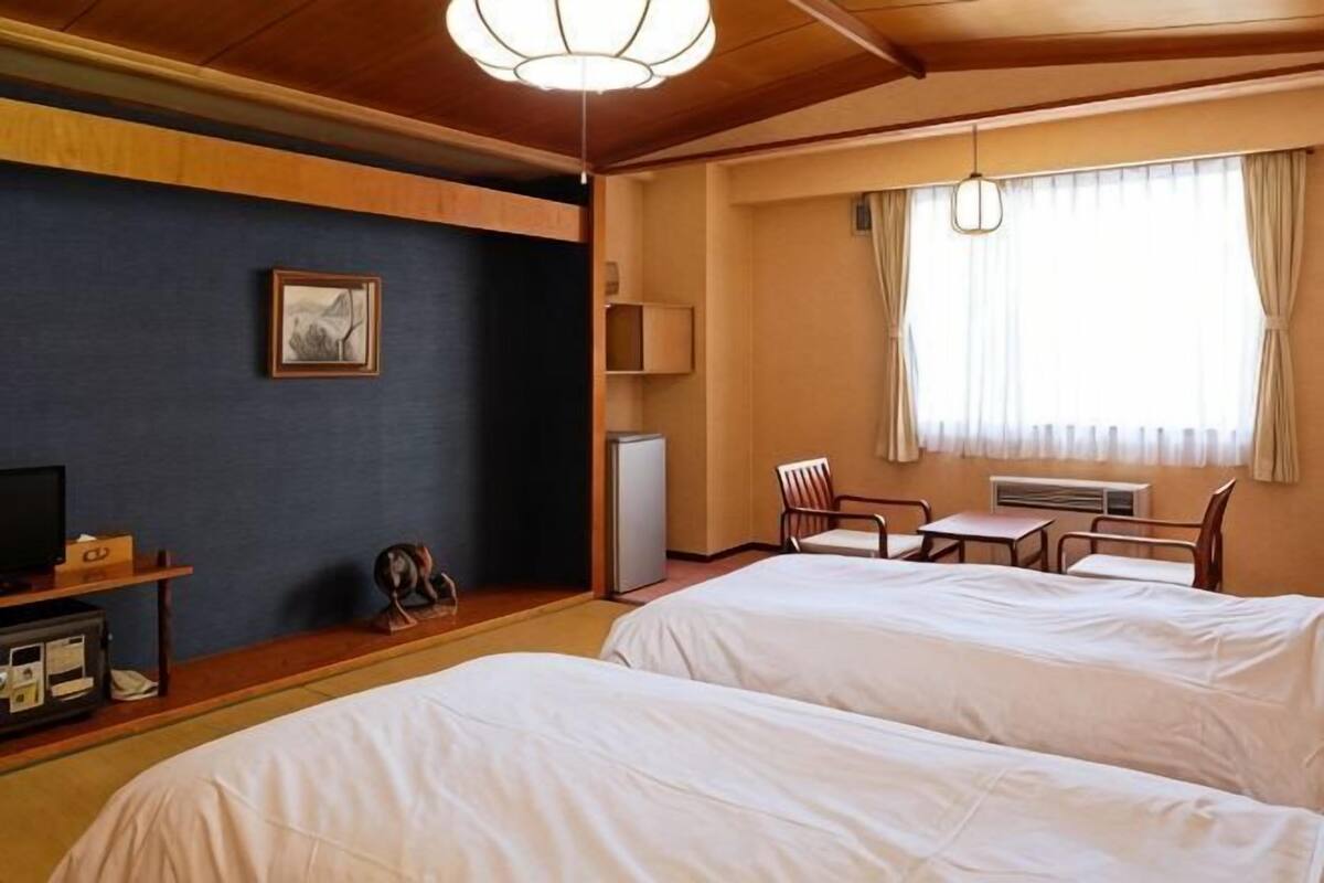 Une chambre d’hôtel avec deux lits, un bureau, une chaise, une télévision et un tableau au mur.