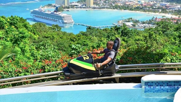 A person on a chairlift with a view of a cruise ship and a coastal town. - Hospitality Expert CPA3: Pool/Beach/Hip-Strip (Montego Bay)