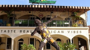 A statue in front of a building with a sign reading "TASTE REAL I CAN VIBES". - Hospitality Expert CPA3: Pool/Beach/Hip-Strip (Montego Bay)