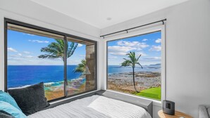A bedroom with a large window offering a view of the ocean and palm trees. - Modern Ocean Views  + AC (Princeville)