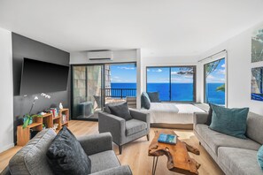 A modern living room with a large flat-screen TV, comfortable seating, a wooden coffee table, and a view of the ocean. - Modern Ocean Views  + AC (Princeville)