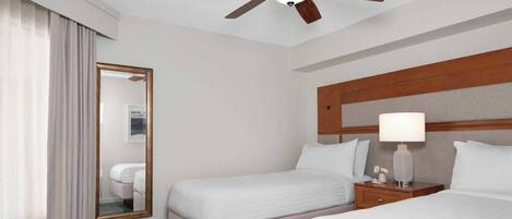 A hotel room with two beds, a ceiling fan, a mirror, a nightstand with a lamp, and a headboard.