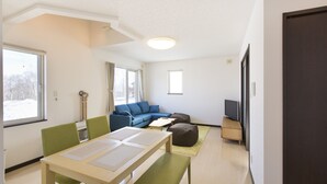 A modern living room with a sofa, a TV, and a dining area with a table and chairs. - Yotei Chalets (Niseko)
