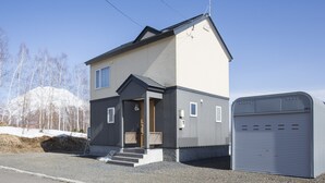 A two-story house with a garage, a front porch, and a driveway. - Yotei Chalets (Niseko)