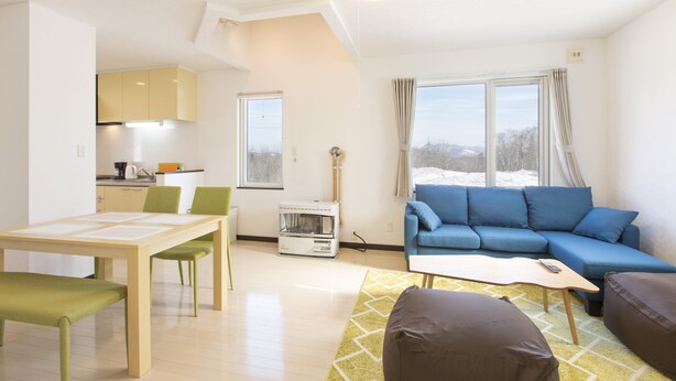 A modern living room with a blue sofa, a wooden coffee table, and a dining area with a table and chairs. - Yotei Chalets (Niseko)