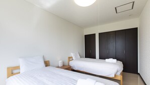 A hotel room with two single beds, a wooden headboard, a nightstand with a lamp, and a dark-colored wardrobe. - Yotei Chalets (Niseko)