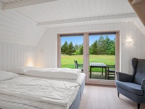 A bedroom with a large bed, a chair, and a view of a grassy area through a glass door.