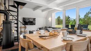 Cozinha moderna com lareira a lenha, mesa de jantar com cadeiras e uma grande janela com vista para o exterior.
