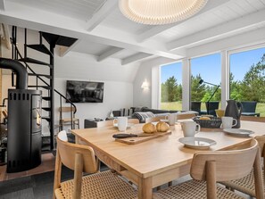 A modern kitchen with a wood-burning stove, a dining table with chairs, and a large window offering a view of the outdoors.
