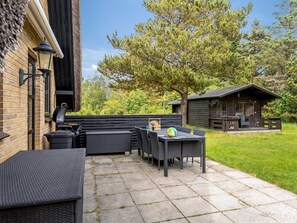 Eine Terrassenausstattung mit Grill, Korbmöbeln und einem Volleyballnetz.