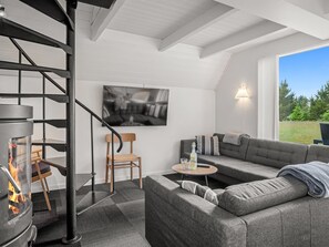 Una sala de estar moderna con chimenea, un sofá, un sillón, una mesita y un televisor montado en la pared.
