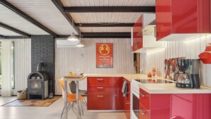 Una cocina moderna con una isla central, muebles rojos y una estufa de leña.