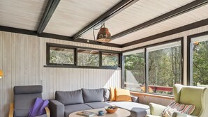 Una sala de estar moderna con un sofá gris, un sillón verde y una mesa de centro. Amplias ventanas ofrecen vistas al exterior.