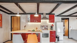 Una cocina moderna con armarios rojos y blancos, una isla central, dos sillas y un lavamanos de acero inoxidable.