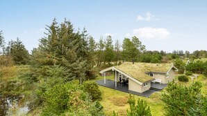 Ein modernes, umweltfreundliches Haus mit Gründach, umgeben von dichtem Wald und einem kleinen Gewässer.