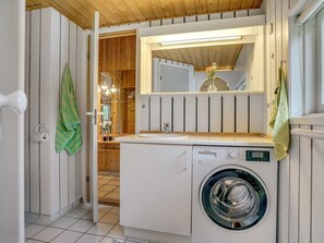 Une petite buanderie équipée d’un lave-linge, d’un miroir au-dessus du lavabo et de lambris en bois sur les murs.