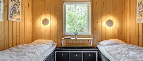 Una cabaña con dos camas, una ventana que da a los árboles y luces fijadas a la pared.