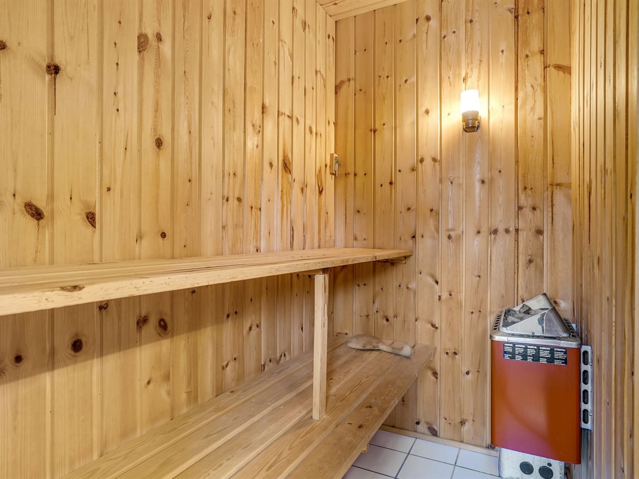 Interior de uma cabana de madeira com uma prateleira, um aquecedor e um candeeiro fixado na parede.