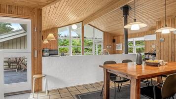 Un intérieur en bois avec un coin repas, un mur en briques blanches et de grandes fenêtres.