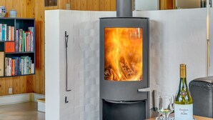 Ein modernes Wohnzimmer mit Kaminofen, Bücherregal und einer Weinflasche auf einem Tisch.