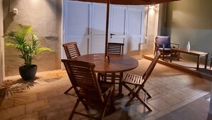 Une terrasse extérieure avec une table ronde en bois, deux chaises, un grand parasol et une plante en pot.
