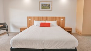 A neatly arranged bedroom with a large bed, a wooden headboard, two bedside tables, a chair, and a framed picture on the wall.