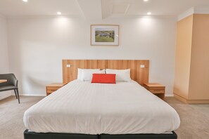 A neatly arranged bedroom with a large bed, a wooden headboard, two bedside tables, a chair, and a framed picture on the wall.