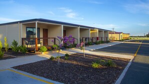 A motel with a covered outdoor seating area, a parking lot, and a row of rooms.