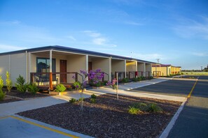 A motel with a covered outdoor seating area, a parking lot, and a row of rooms.