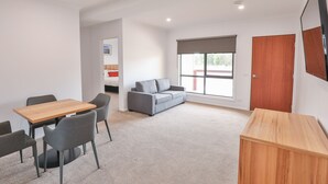 Een moderne kamer met een houten tafel en stoelen, een grijze bank en een groot raam met uitzicht.