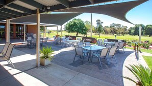 An outdoor patio area with tables and chairs, a covered seating area, and a view of a golf course.