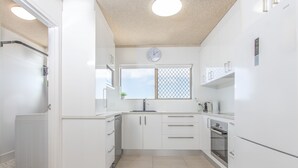 Une cuisine moderne avec des meubles blancs, un four encastré et une fenêtre ornée d’une grille métallique.