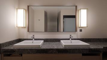 A modern bathroom with two sinks, a large mirror, and wall-mounted lights.